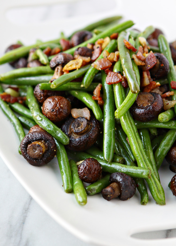 sauteed green beans with bacon on a white plate on a white marble counter