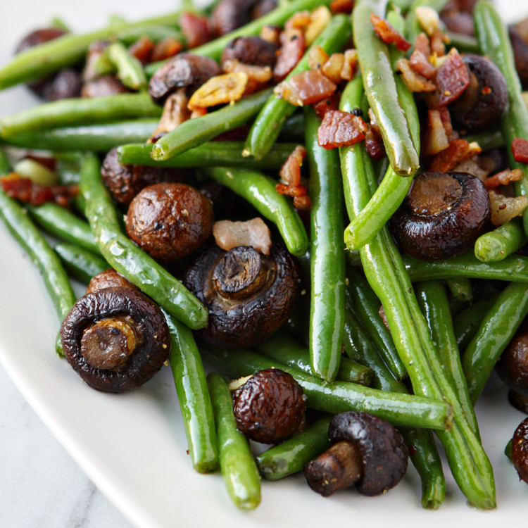 sauteed green beans with bacon on a white plate on a white marble counter