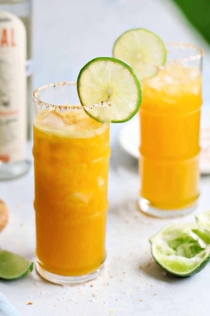 two passion fruit margaritas on a light blue background with slices of lime