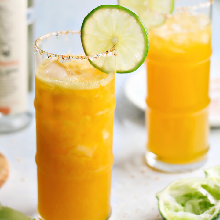 two passion fruit margaritas on a light blue background with slices of lime