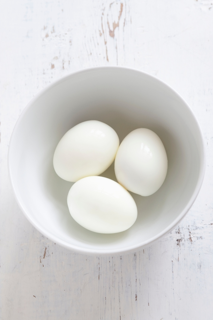 white bowl with peeled hard boiled eggs on a white wooden background