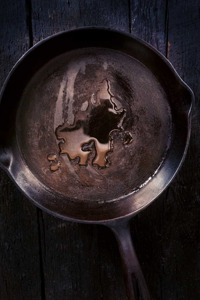 overhead shot of a cast iron skillet with oil in it on a dark background