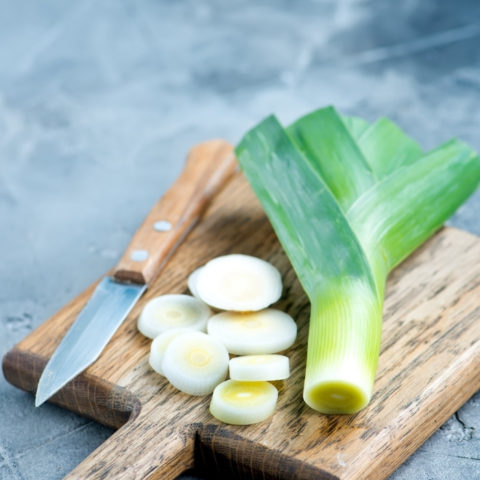 leeks on a wooden cutting board with a knife