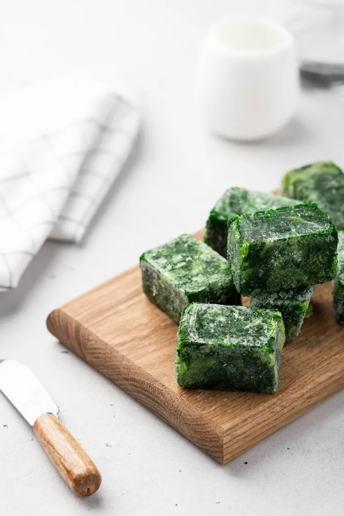 frozen cubes of spinach on a cutting board with white background