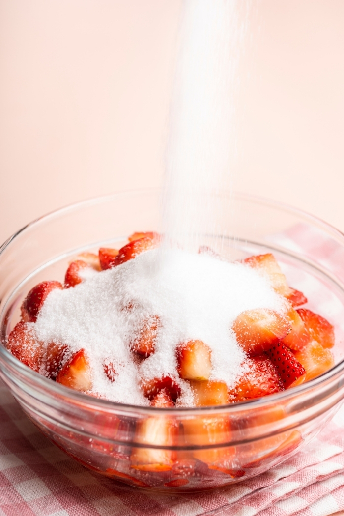 pouring sugar into a bowl of sliced strawberries to make strawberries and cream