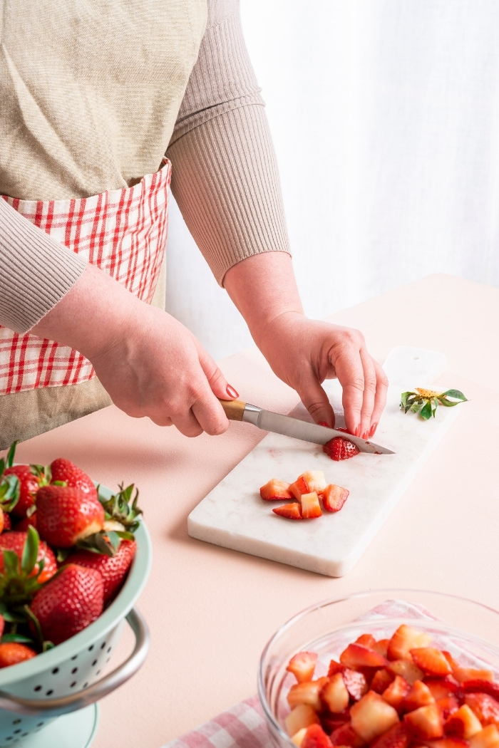 woman slicing strawberries on a cutting board to make strawberries and cream