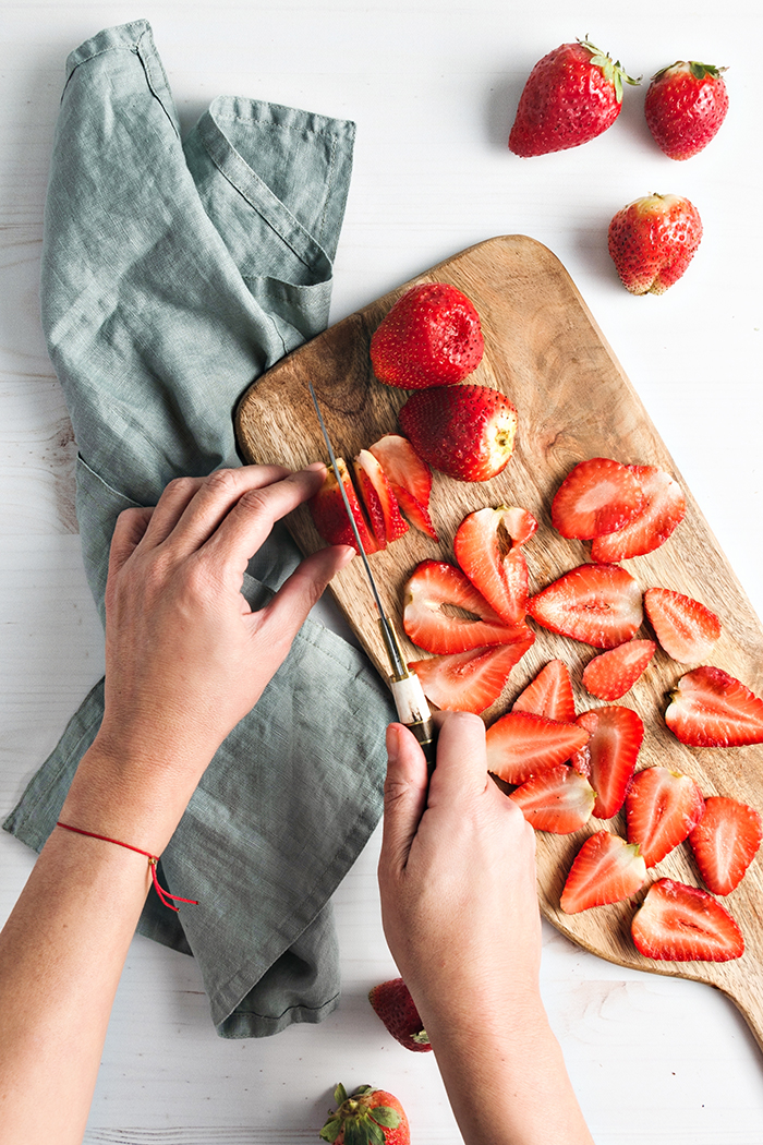 slicing strawberries with a knife on a wooden cutting board