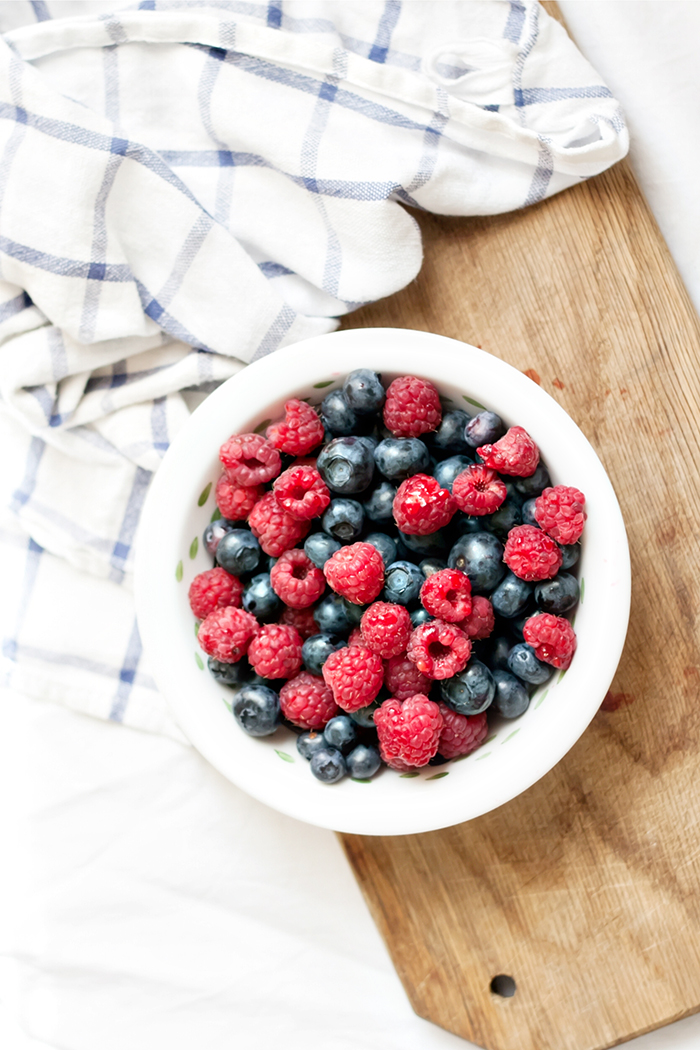 white bowl of raspberries and blueberries on a cutting board
