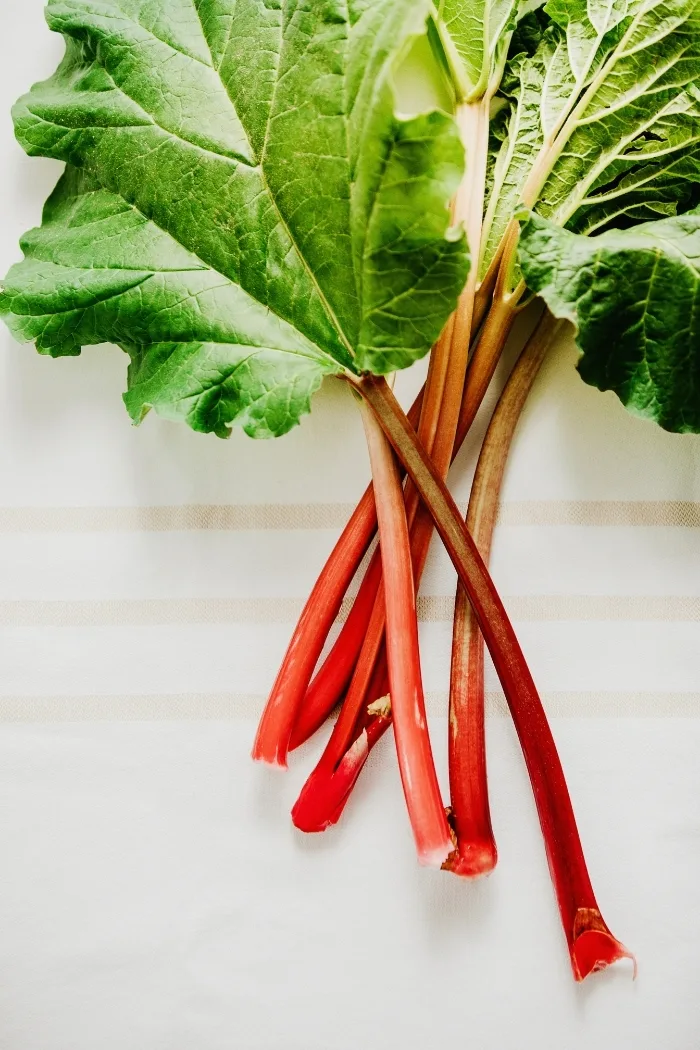 overhead shot of fresh rhubarb stalks with leaves attached on a white tablecloth