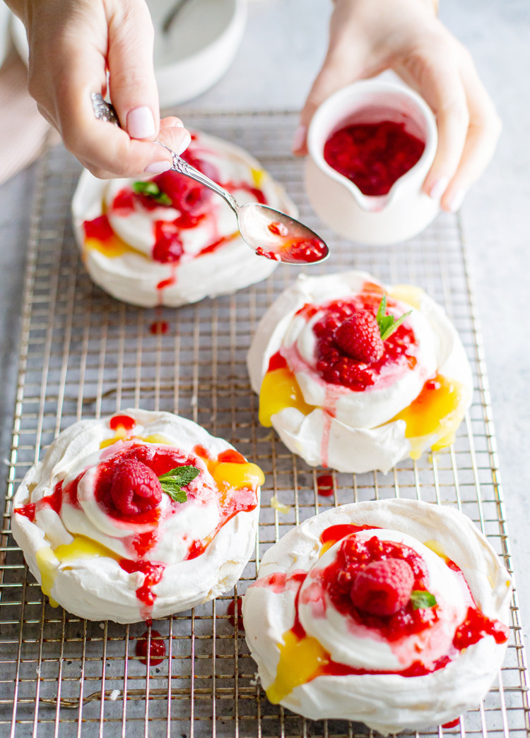 woman spooning raspberries onto lemon curd pavlova