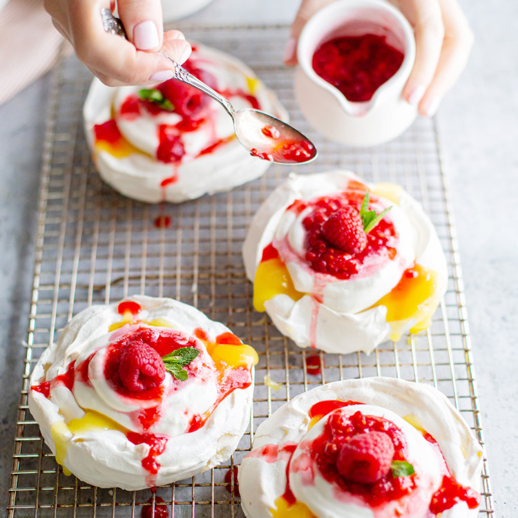 woman spooning raspberries onto lemon curd pavlova