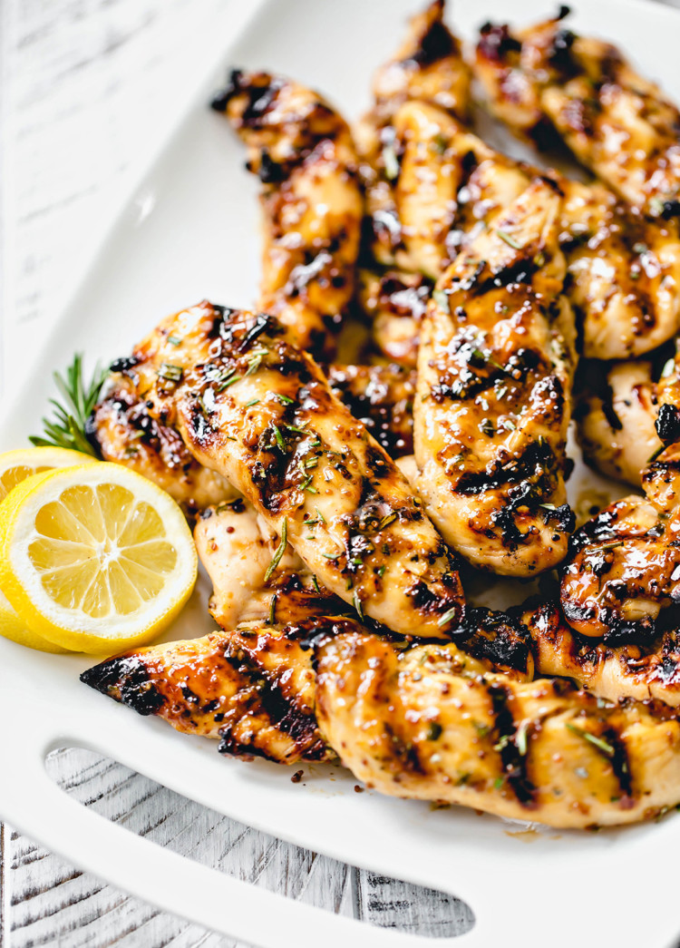 white platter with grilled honey mustard chicken next to fresh rosemary and lemon slices