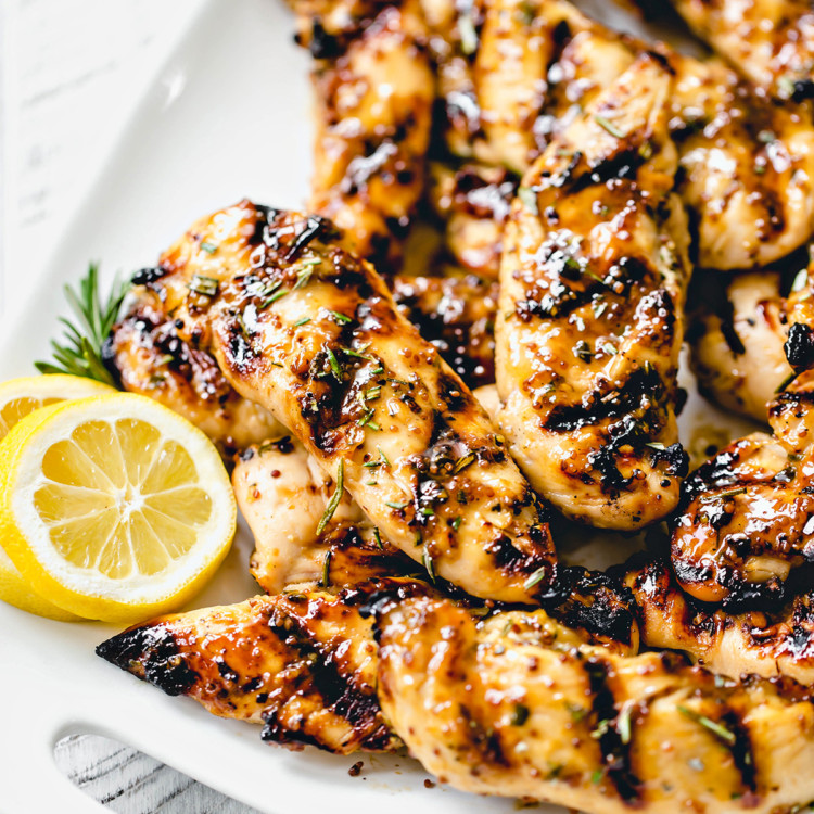 white platter with grilled honey mustard chicken next to fresh rosemary and lemon slices