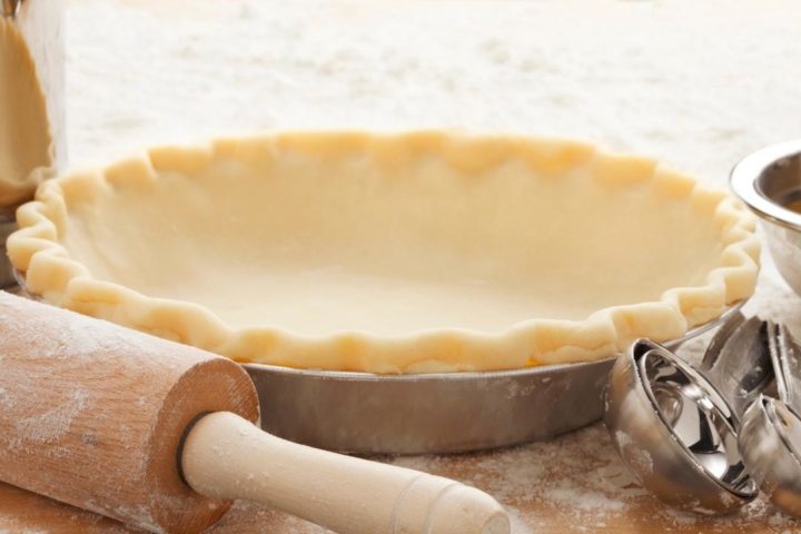 photo of a pie crust recipe with butter in a pie plate unbaked next to a rolling pin