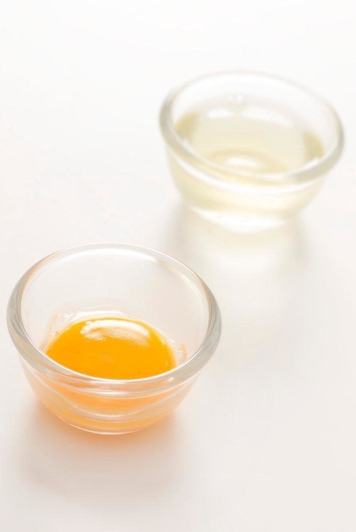 egg yolk in a glass bowl in front of egg white in a glass bowl