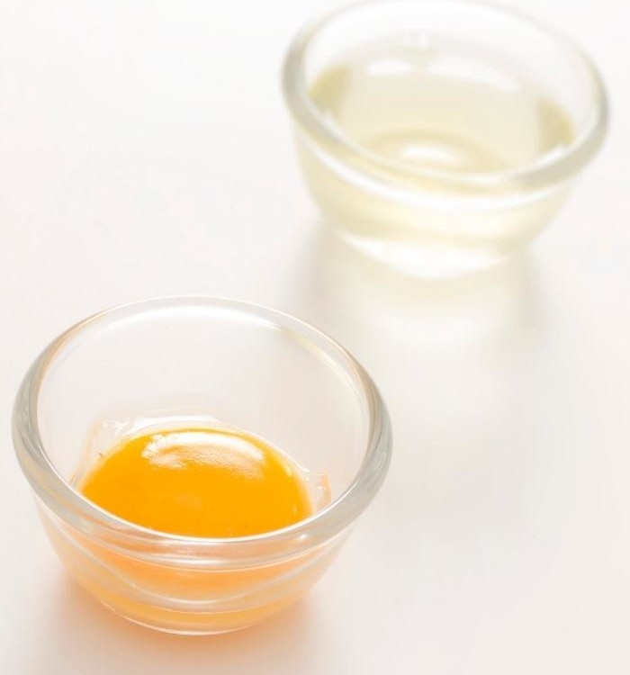 egg yolk in a glass bowl in front of egg white in a glass bowl