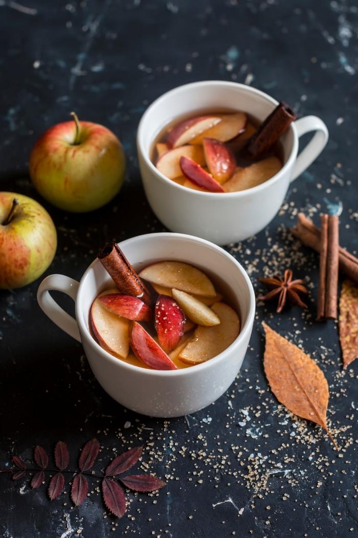 mugs of hot apple cider with apple slices and cinnamon stick