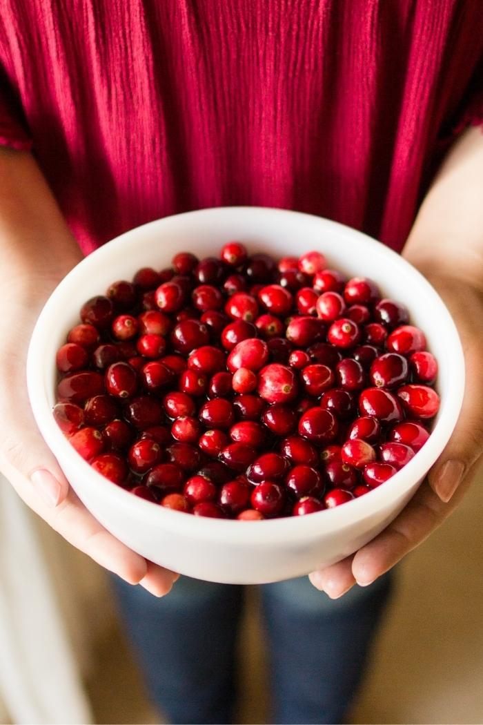 woman with red shirt holding a white bowl of cranberries