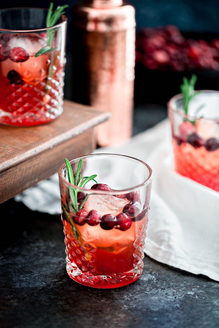 photo of a shrub cocktail in low ball glasses with rosemary and cranberry garnishes