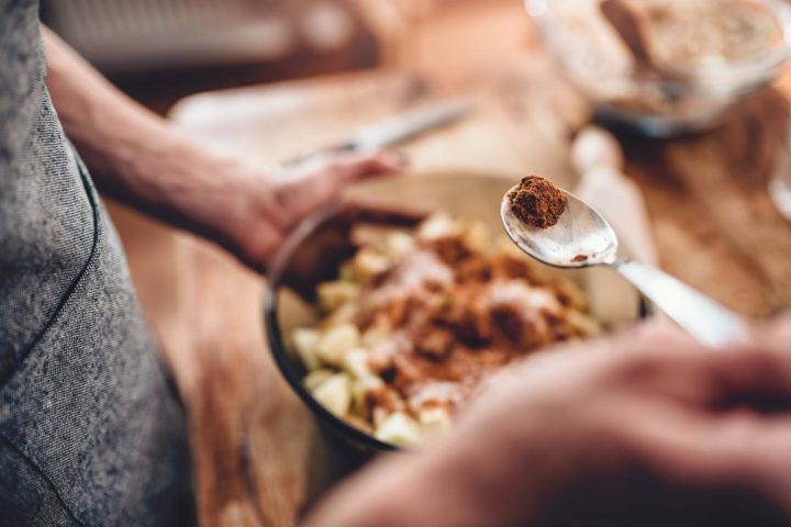 woman adding cinnamon to apple pie ingredients