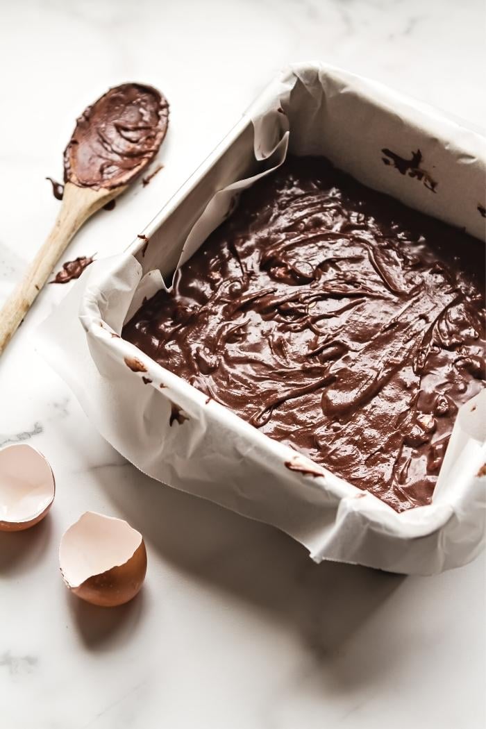 homemade brownie batter in a parchment paper lined pan