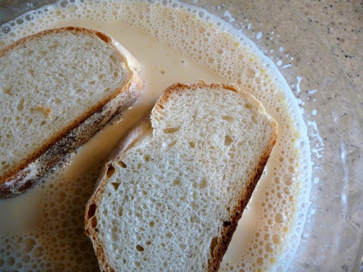 Two pieces of bread being soaked in an egg-milk mixture.