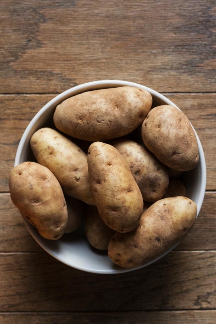 photo of a bowl of russet potatoes on a wooden table to use in this recipe for Parmesan mashed potatoes with brown butter