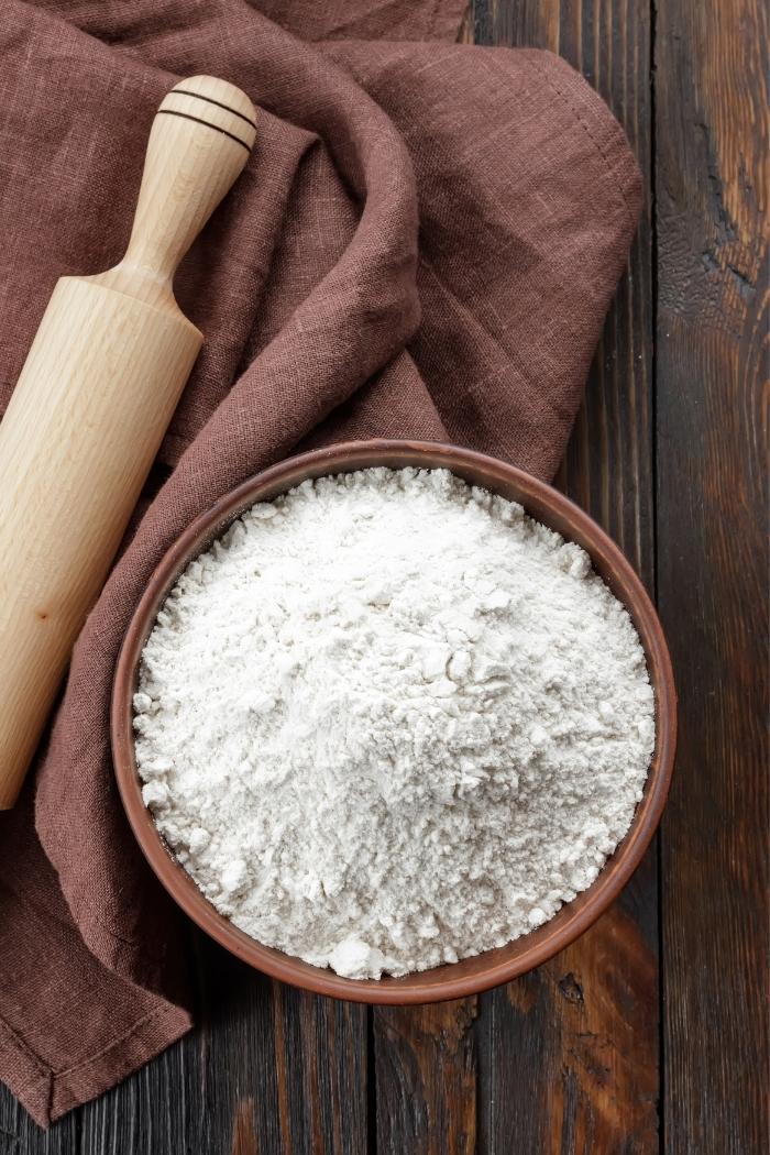 bowl of flour on rustic background with rolling pin