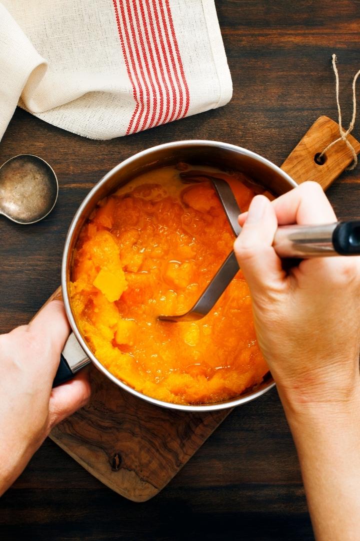 person mashing pumpkin puree in a pot