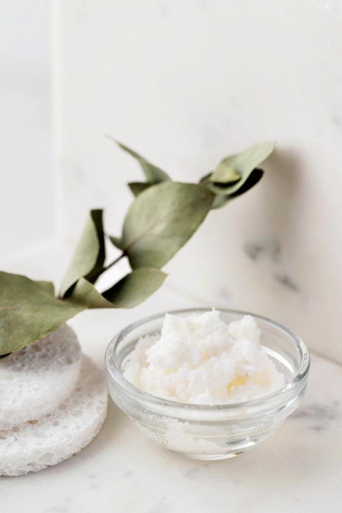 clear bowl of rosemary mint sugar scrub on a marble counter