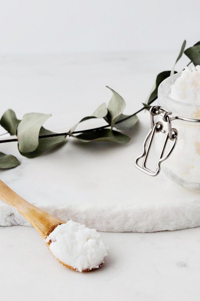 jar of rosemary mint sugar scrub on a marble counter with a wooden spoon