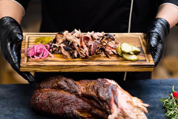 a photo of smoked pork shoulder on a counter in front of a man holding a cutting board with traeger pulled pork on it