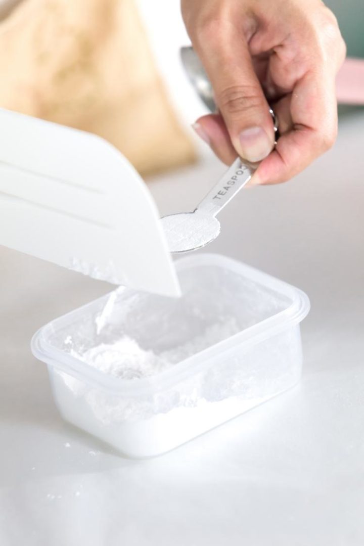 person measuring baking powder with a teaspoon