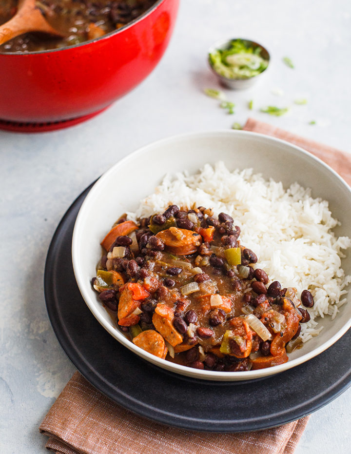 bowl of black beans and rice with sausage on a table next to a red pot