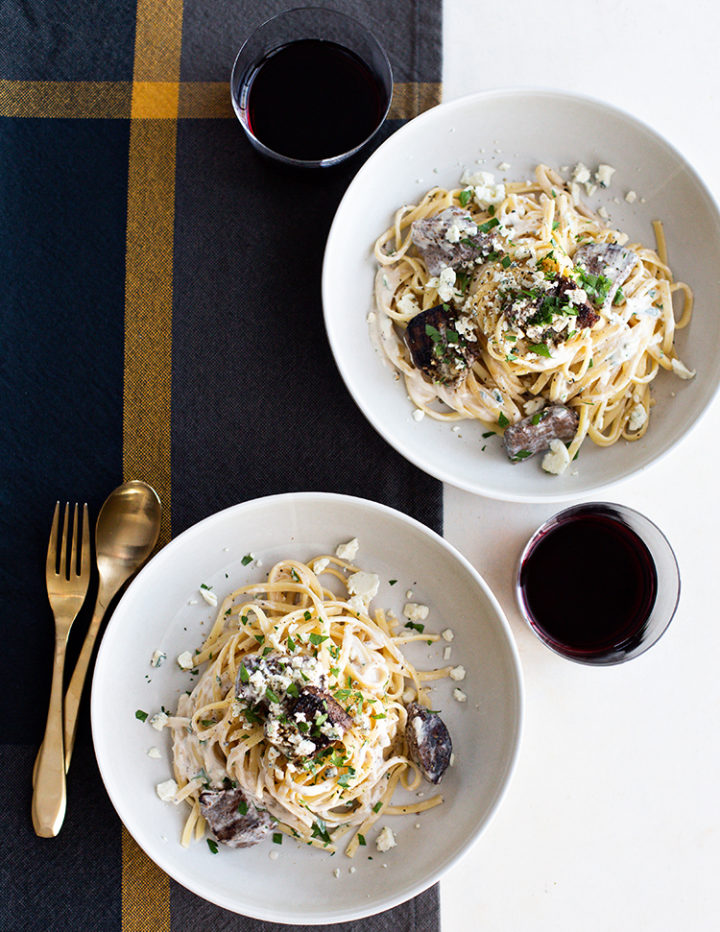 overhead shot of gorgonzola pasta with beef tenderloin in white bowls with glasses of wine