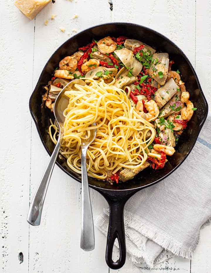 cast iron pan with shrimp scampi and linguine on a white farmhouse table