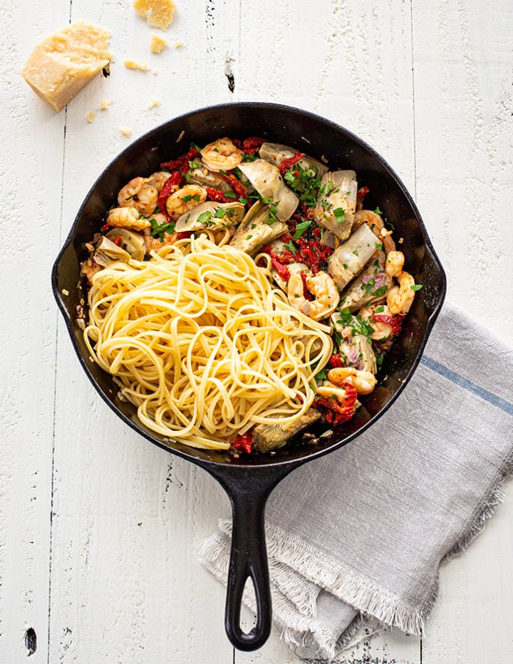 cast iron pan with shrimp scampi and linguine on a white farmhouse table