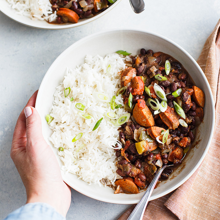 overhead shot of bowl with black beans and rice and woman's hands