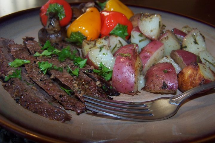 photo of rosemary grilled red potatoes on a plate with flank steak, bell peppers, and mushrooms