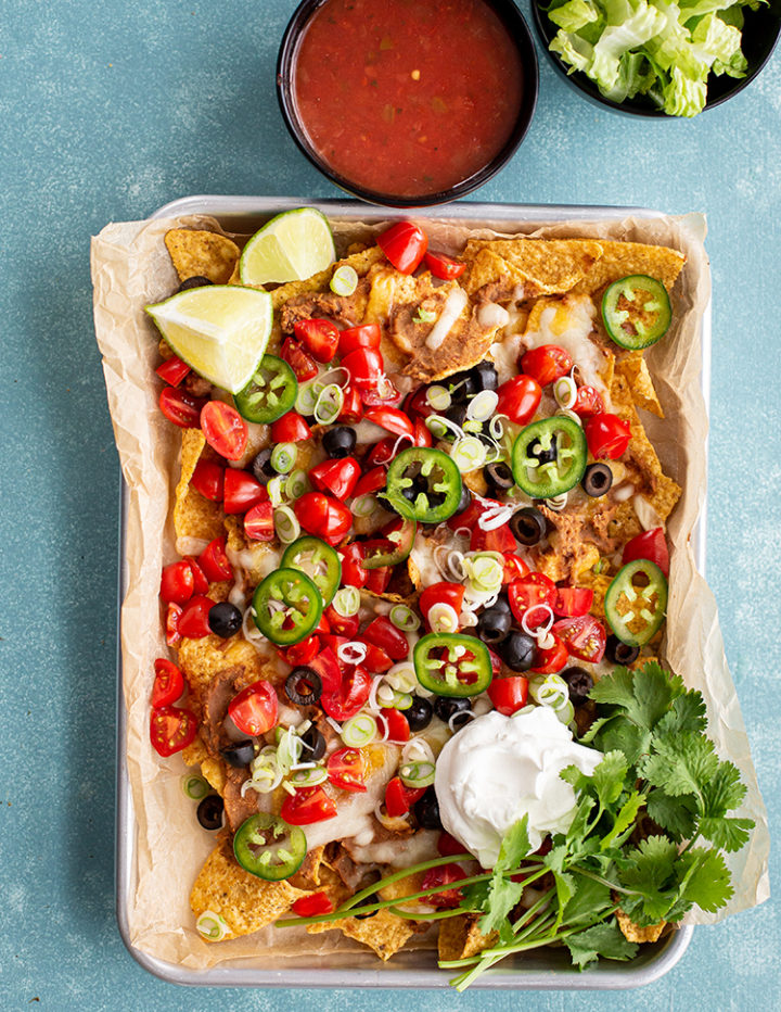 overhead photo of this baked nachos recipe on a baking sheet with a blue background