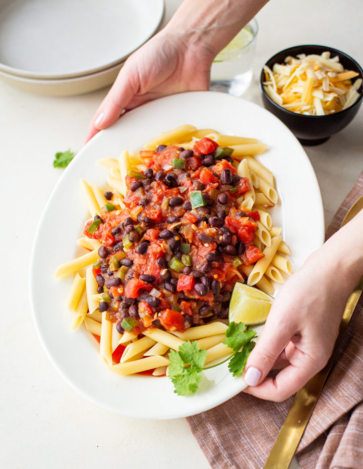 woman setting the table with a white platter of pasta with black beans