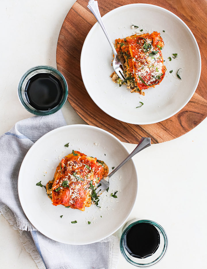 overhead photo of lasagna slices on two white plates with forks and glasses of wine