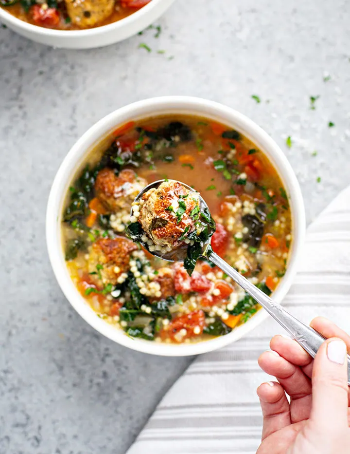 woman holding a spoon with a meatball in it over a white bowl with italian wedding soup