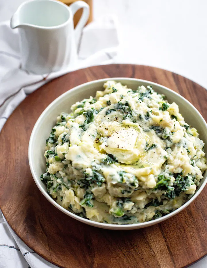 white bowl of irish mashed potatoes (colcannon with leek and kale) on a wooden tray