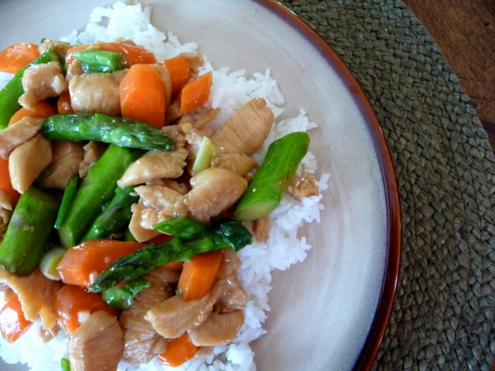 a plate of rice with chicken asparagus stir fry on top