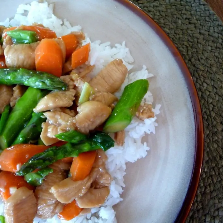 overhead shot of chicken asparagus stir fry on a bed of rice on a brown plate
