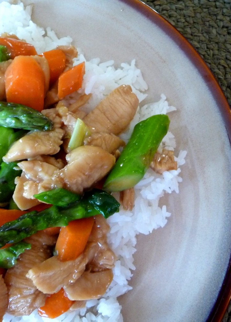 overhead shot of chicken asparagus stir fry on a bed of rice on a brown plate