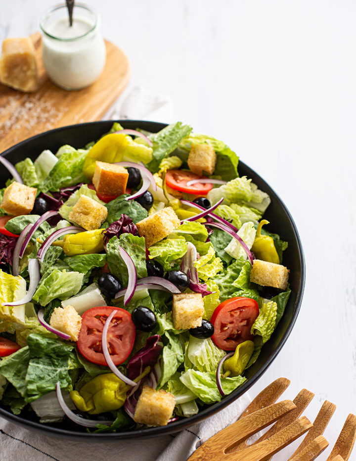 overheat shot of a bowl of olive garden salad recipe with olive garden dressing in the background