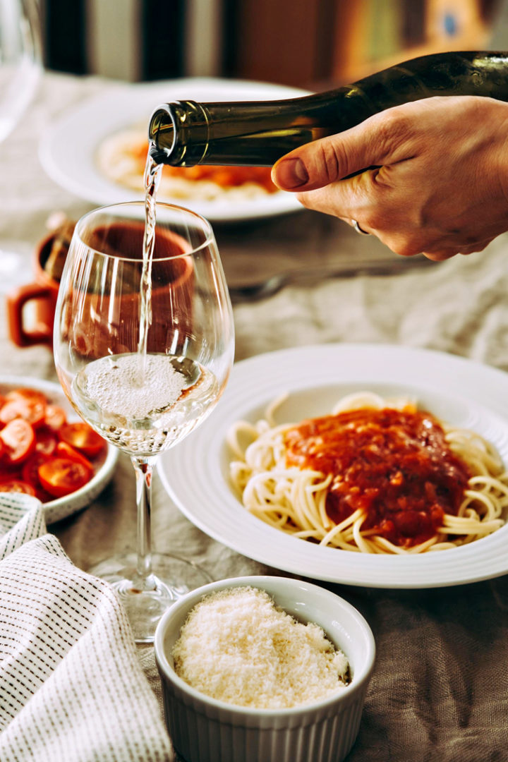 pouring a glass of wine next to a bowl of spaghetti