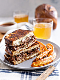 photo of a french dip panini on a plate with sweet potato fries and a glass of beer